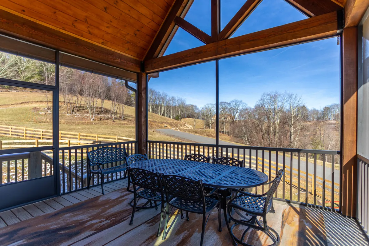A spacious outdoor dining table sits beneath wooden beams, with panoramic views of the surrounding landscape visible through large windows. The scene is filled with natural light and offers a seamless connection between the indoor comforts and the natural mountain setting—ideal for festive dinners, morning coffee, or starry nights.