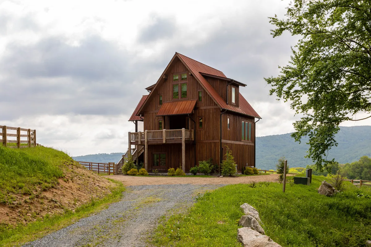 This exterior image features the Eagles Nest house nestled in a serene landscape with mountains in the background and a winding driveway leading up to the property. The setting exudes tranquility and hints at the vast grounds and natural beauty surrounding the home, inviting guests to explore outdoor adventures year-round.