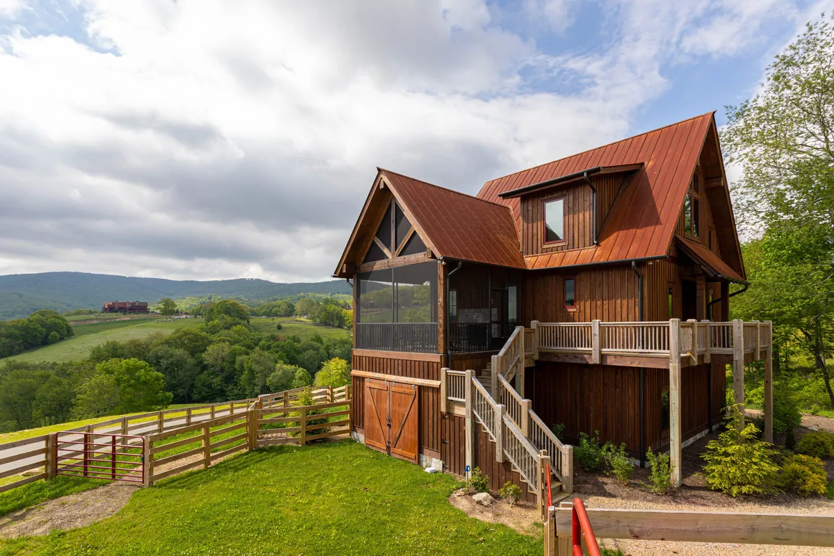 A welcoming wooden structure with a red metal roof and a spacious deck, set within a serene landscape. The deck area is perfect for outdoor gatherings, relaxing after a day of adventure, or cozy fireside moments in the fresh mountain air.