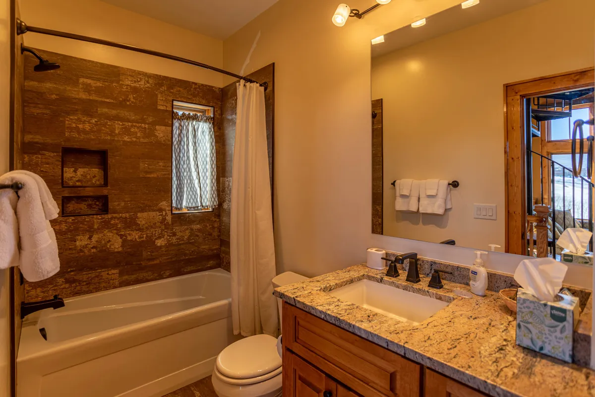 This image features a full bathroom with a granite countertop, textured wall, and a window with a patterned curtain. The mood is calm and serene, inviting guests to refresh and relax after gatherings.