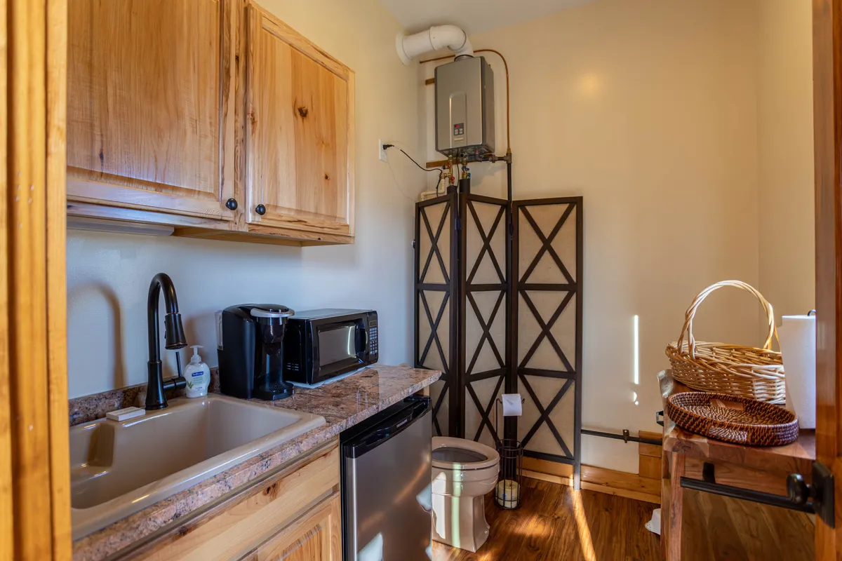 This interior image highlights a practical zone with a sink, microwave, refrigerator, and wooden cabinetry. The setup is functional and versatile, suggestive of a space where laundry duties, meal prep, and efficient routines intersect—ideal for both equestrian guests needing a spot for muddy boots and families storing adventure gear.